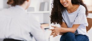 A woman smiles while sitting across from a person with a clipboard. This could represent the support offered from a trauma-informed consultant in Baltimore, MD. Learn more about holistic healing in Balitmore, MD by searching for holistic healing in baltimore, MD today.