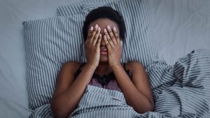A woman covers her face with her hands while laying in bed. A trauma therapist in Baltimore, MD can offer support in addressing past pain and teach coping skills. Contact a black therapist in Baltimore or search for trauma healing in Baltimore, MD today.