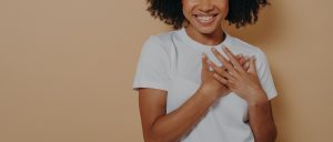 A close up of a woman smiling with her hand over her heart. This could represent the importance of a whole body approach to mental health. Learn more about integrative mental health in Baltimore, MD by searching for a certified integrative mental health professional in Baltimore, MD. 