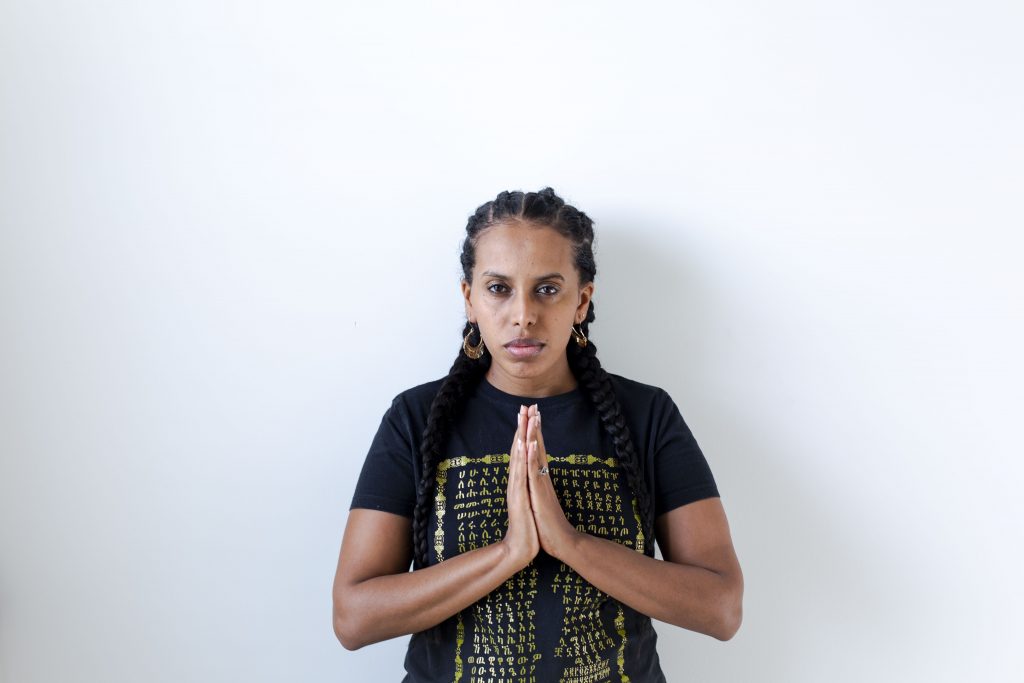 A strong black woman stands with her hands palm together in front of her. She is a survivor of racial trauma in Baltimore, MD.