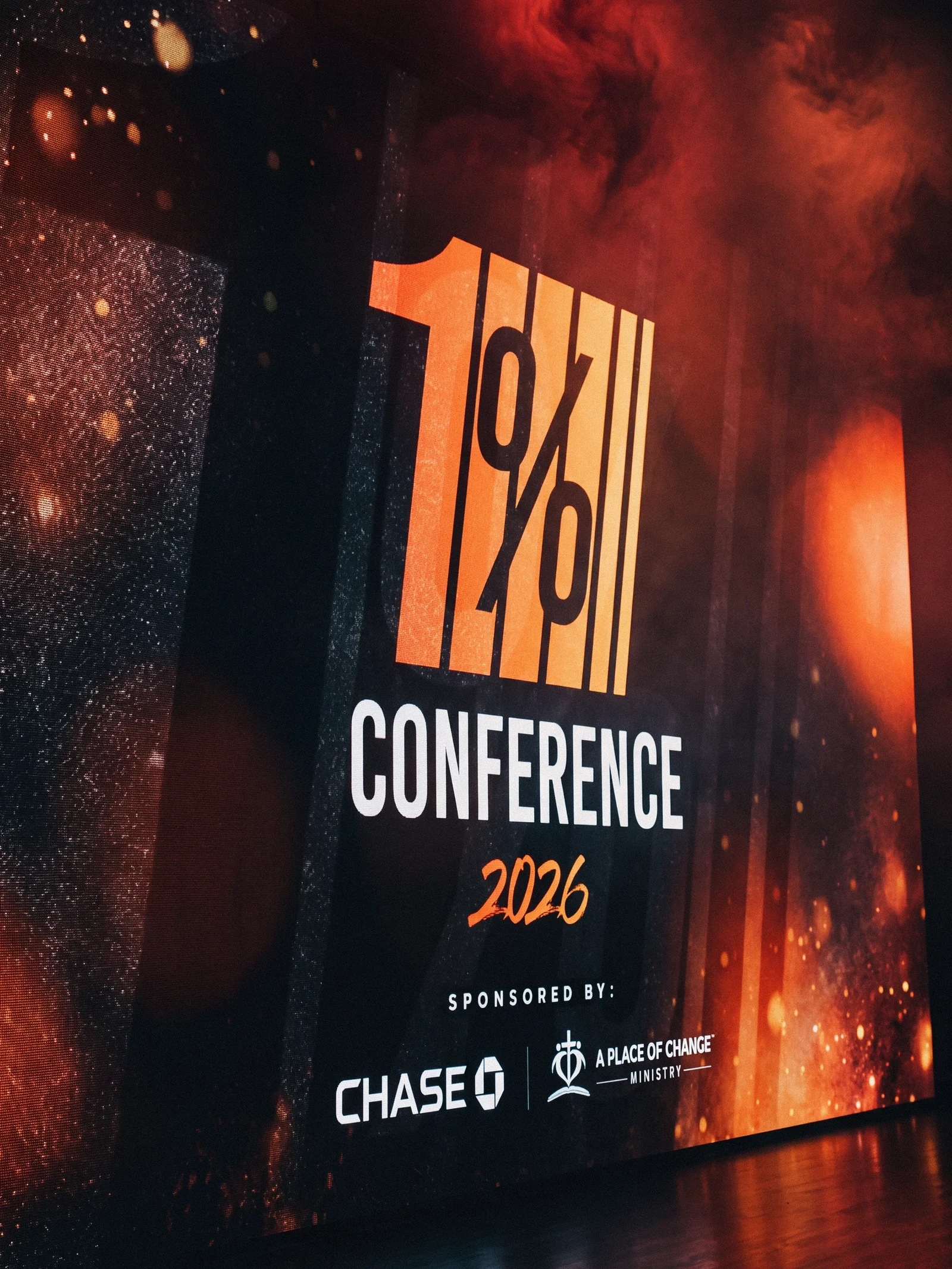 1% Conference stage branding in orange, black, and white.
