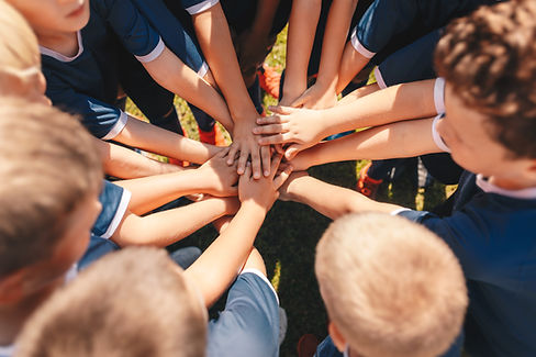 Happy kids sports team stacking hands at the field. Children team sports. Boys at sports c