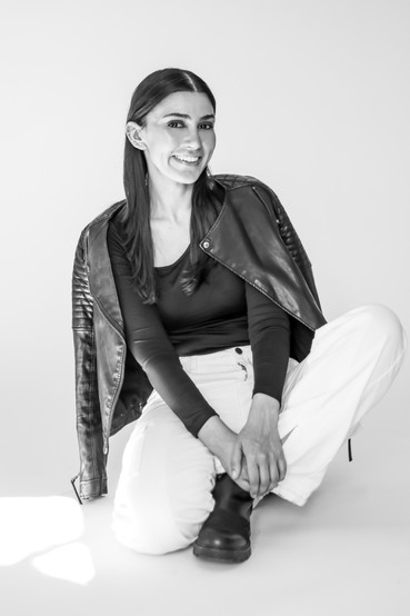 A young woman posing for a portrait. She is sitting casually, laughing with a leather jacket thrown over her shoulder.