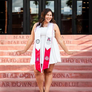 Graduate smiling in white dress and red stole on iconic Bear Down steps at U of A