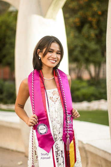Girl smiling and posing at camera while showing off her colorful grad stoles by holding them out. Tucson Grad Pictures U of A