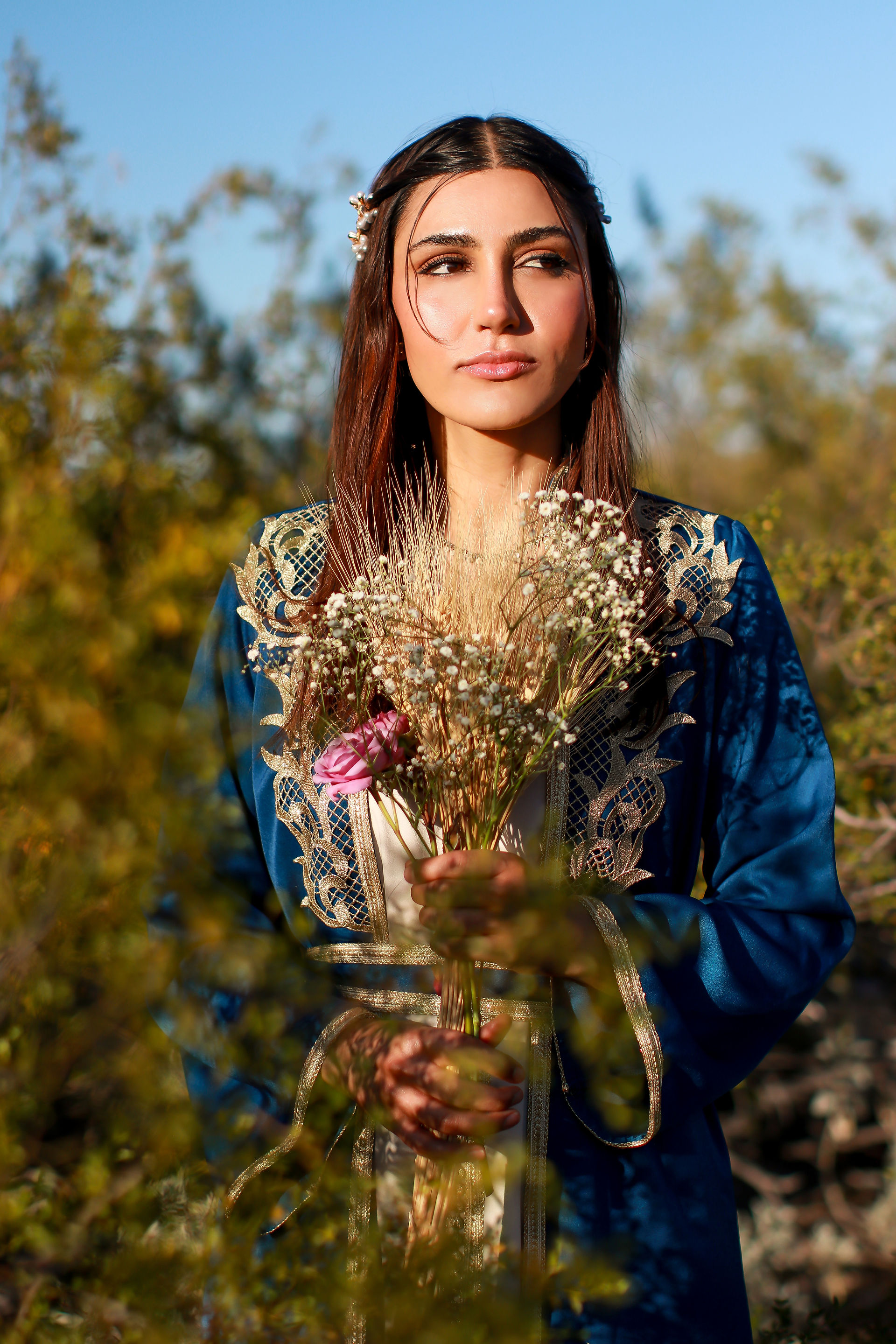 A woman walking in the Tucson desert turns to stare off toward the setting sun. She holds a bouquet of roses and dried flowers