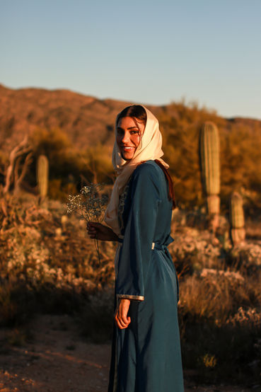 A woman walking in the Tucson desert turns to stare off toward the setting sun. She holds a bouquet of baby's breath