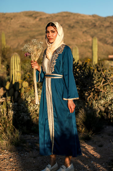 A woman walking in the Tucson desert turns to stare off toward the setting sun. She holds a bouquet of flowers