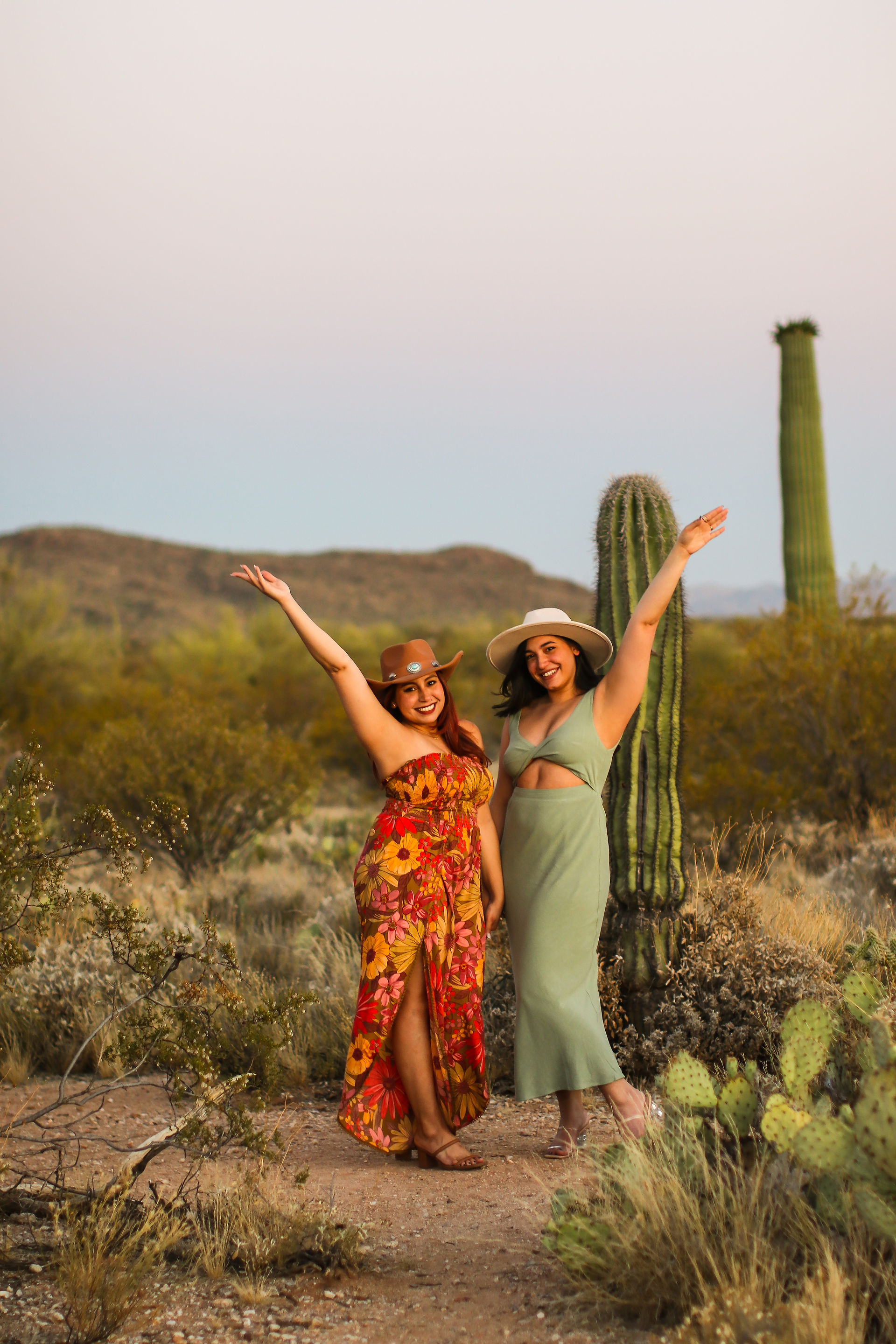 Two sisters hold their arms up in celebration as they walk through the Tucson desert among cacti