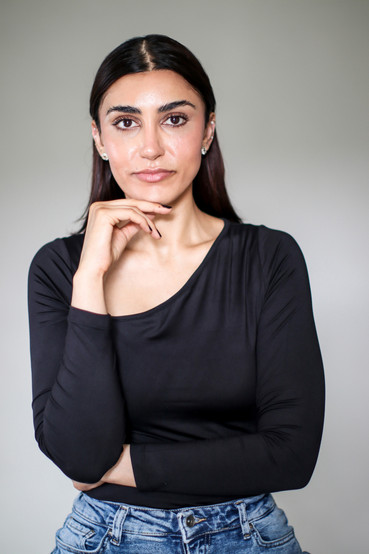 A young woman posing with her hand resting under her chin looking directly in the camera. She is posing for a professional headshot.