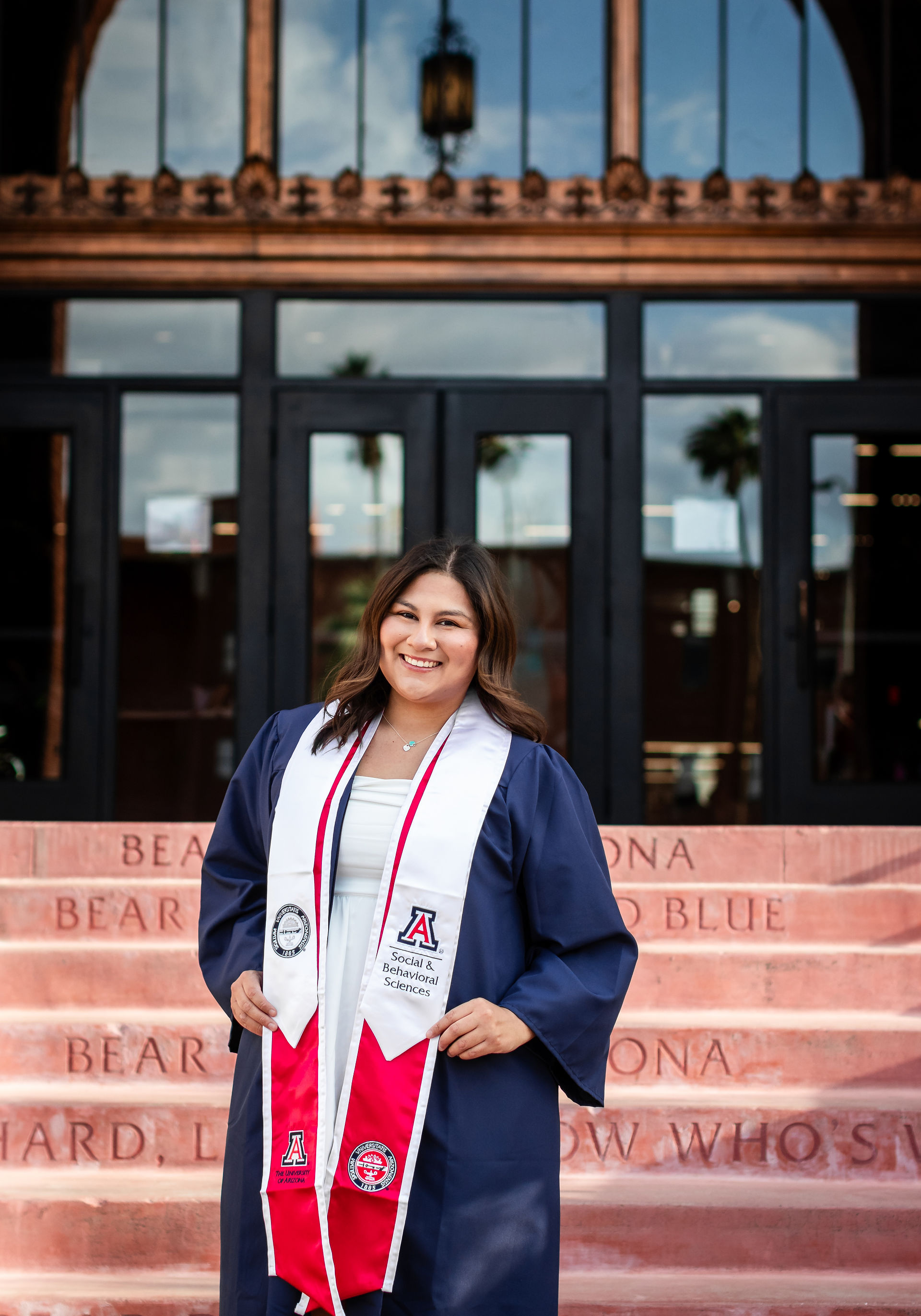 University of Arizona graduate smiling in front of Old Main steps wearing cap and gown