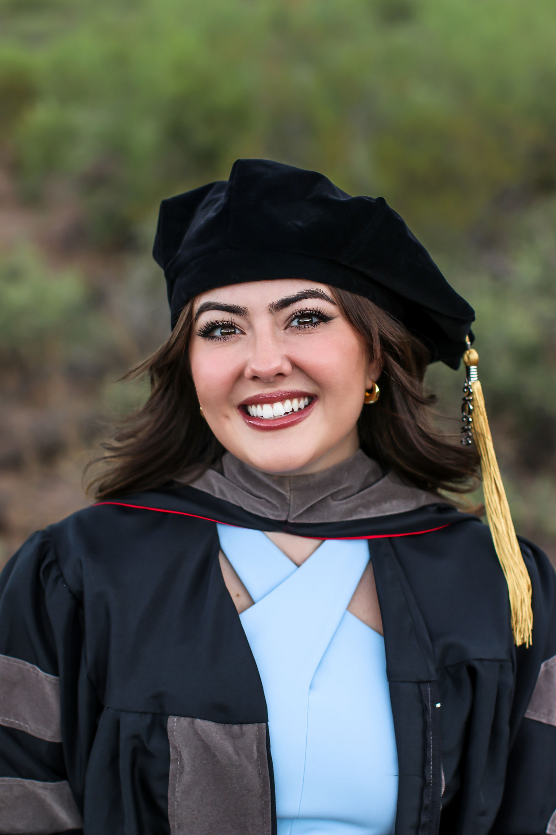 During a graduate photo session a woman smiles for a headshot wearing graduation regalia. 