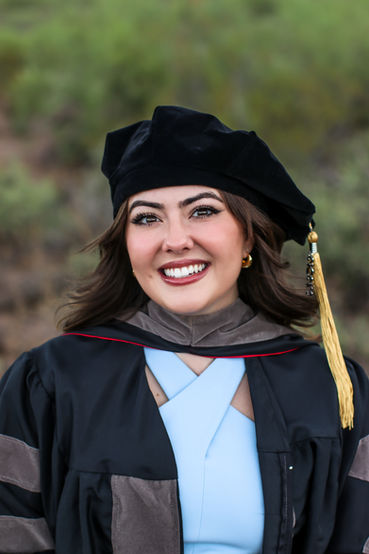 During a graduate photo session a woman smiles for a headshot wearing graduation regalia. 