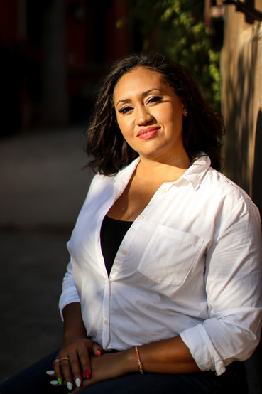 An astrologer sits outside in the sun, smiling as she works on her computer.