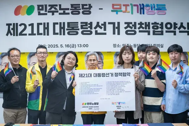 (Text alternatiu. Al centre, el candidat Kwon Young-gook del Partit Democràtic del Treball, sostenint un cartell amb el títol de l’acte «Acord polític per a la 21ra elecció presidencial». Als seus costats, persones representants de l’Acció Arc del Cel amb banderes arc del cel a les seves mans. Al fons una pancarta amb el mateix títol de l’acte.) (Font: Hankyoreh, https://www.hani.co.kr/arti/politics/election/1197947.html)