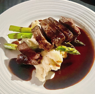 a plate of cut beef with gravy, vegetables, and mashed potatoes