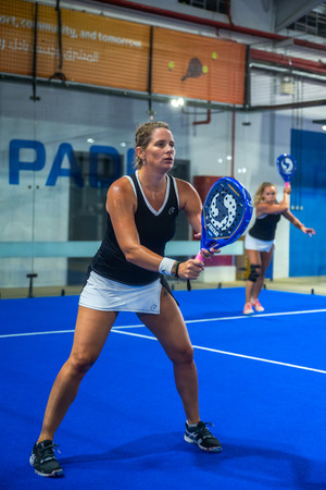 Focused female player waiting for serve on an indoor paddle tennis court