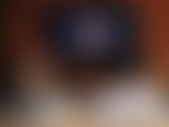 Two people sit on a couch watching Netflix on a wall-mounted TV in a cozy room with a red brick wall and wooden shelves.