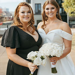 Two women with elegant event hair styling, holding white bouquets
