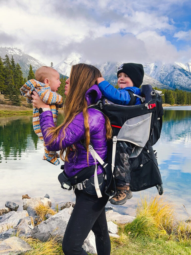 Adrianna holds one son in her arms, while the older one is on her back in a Osprey Poco Plus.