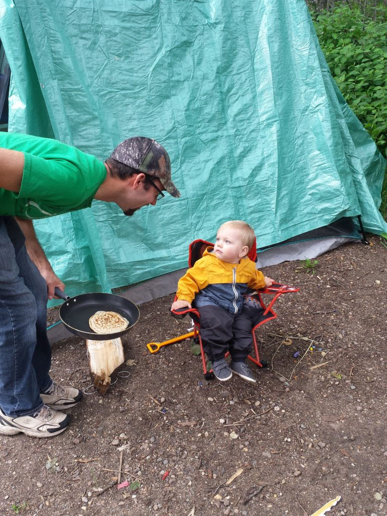 A dad and his young son make pancakes while camping.