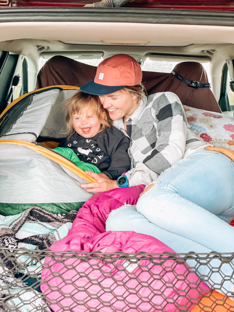 A mom and her young daughter cuddle while car camping.