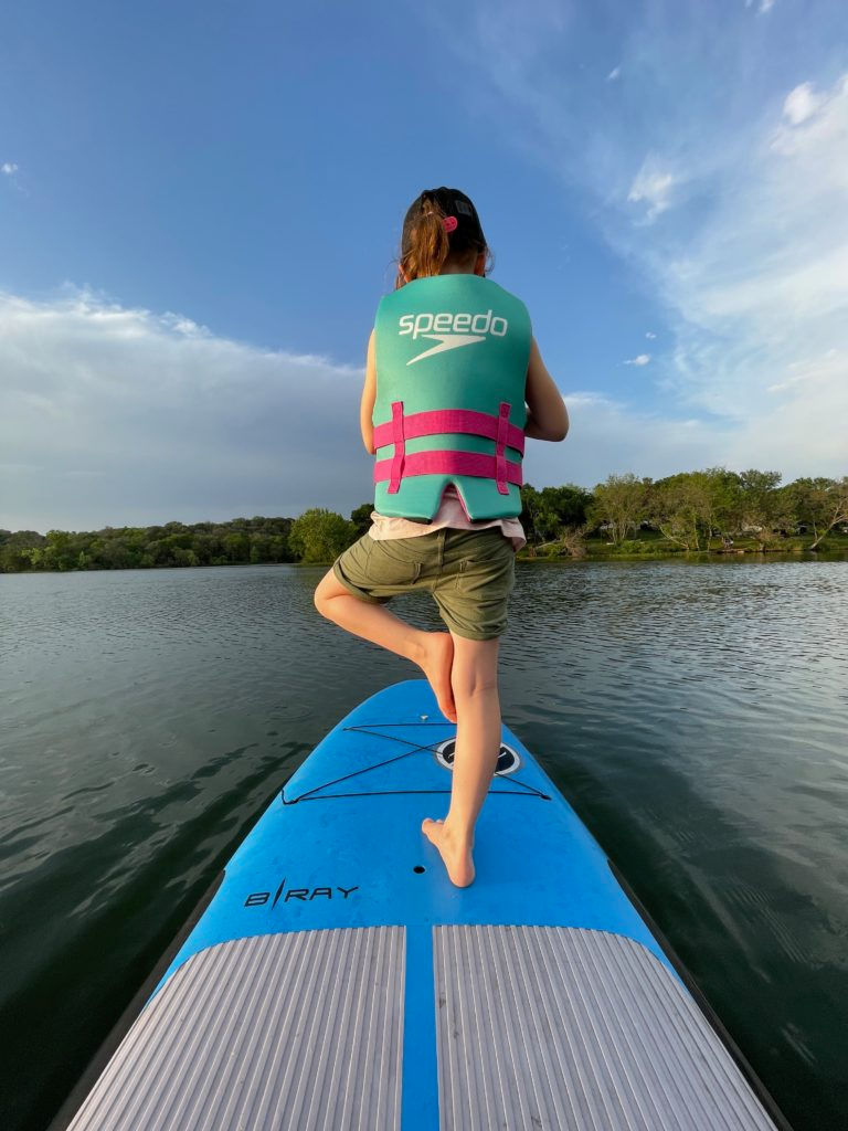 A young girl strikes a yoga pose on a paddle board.