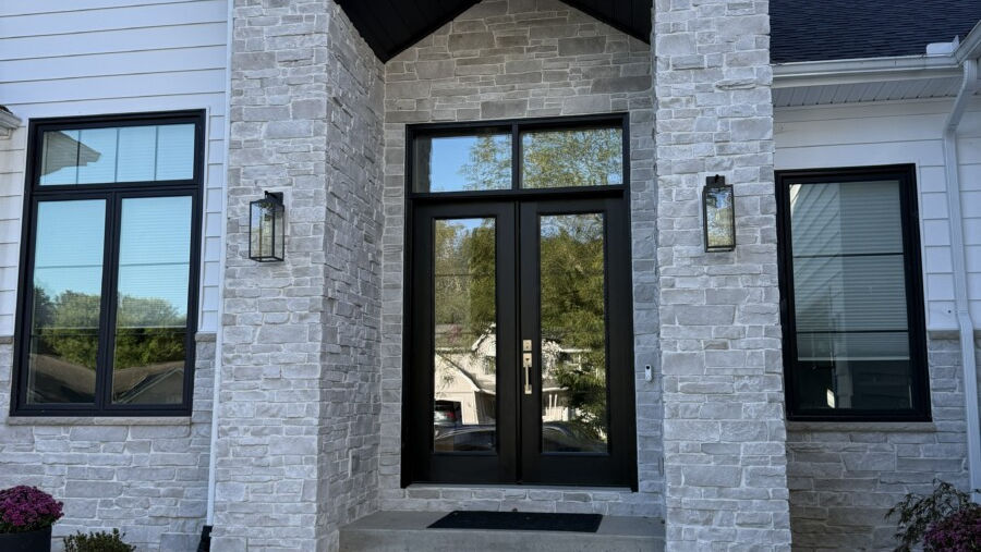 Soft white and very light gray ledgestone with subtle variation creates a bright, clean façade beside high-contrast black windows and trim.