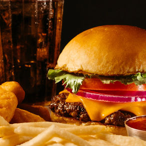 Burger with lettuce, tomato, and onion, beside fries and nuggets. A drink is in the background. Warm, appetizing colors.