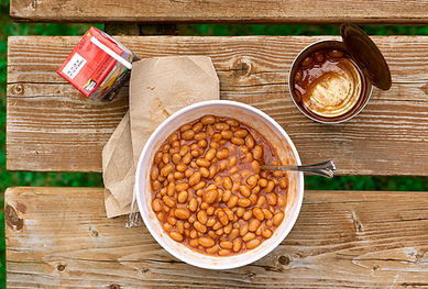 A bowl of beans with a juice box top left and an open nearly empty can top right