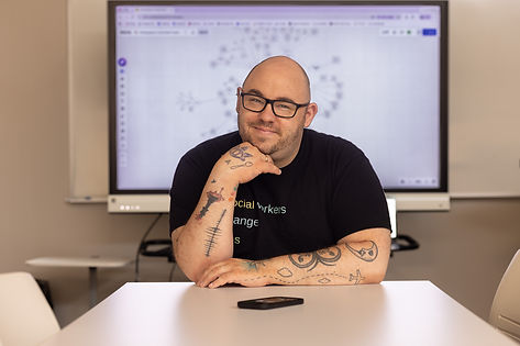 Tim Campbell Smith smiles and looks directly into the camera with a concept map on a tv screen behind him