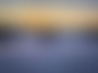 A person walks forth over a snowy landscape into a golden winter sunrise, leaving footprints behind in the snow. 