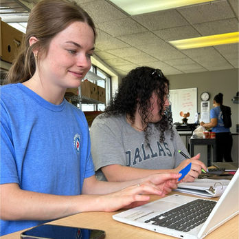 Two women working on laptops at a desk with Dallas on their shirt.