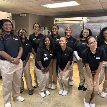 Group smiling in black shirts and khaki pants, Approved Helping Hands, kitchen setting.