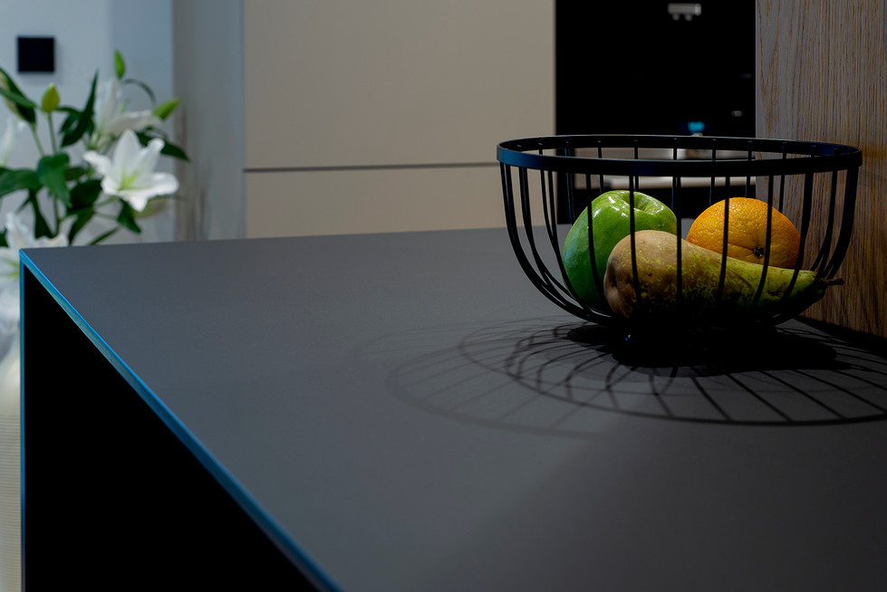 Zwarte draadfruitmand vol fruit op strak donkergrijs aanrechtblad.