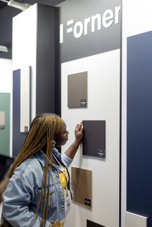 Vrouw met lange vlechten bekijkt "iForner" matte kleurstalen op beursstand.