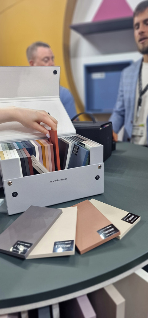 Vrouw kiest kleurstalen uit witte doos 'www.forner.pl' op tafel.