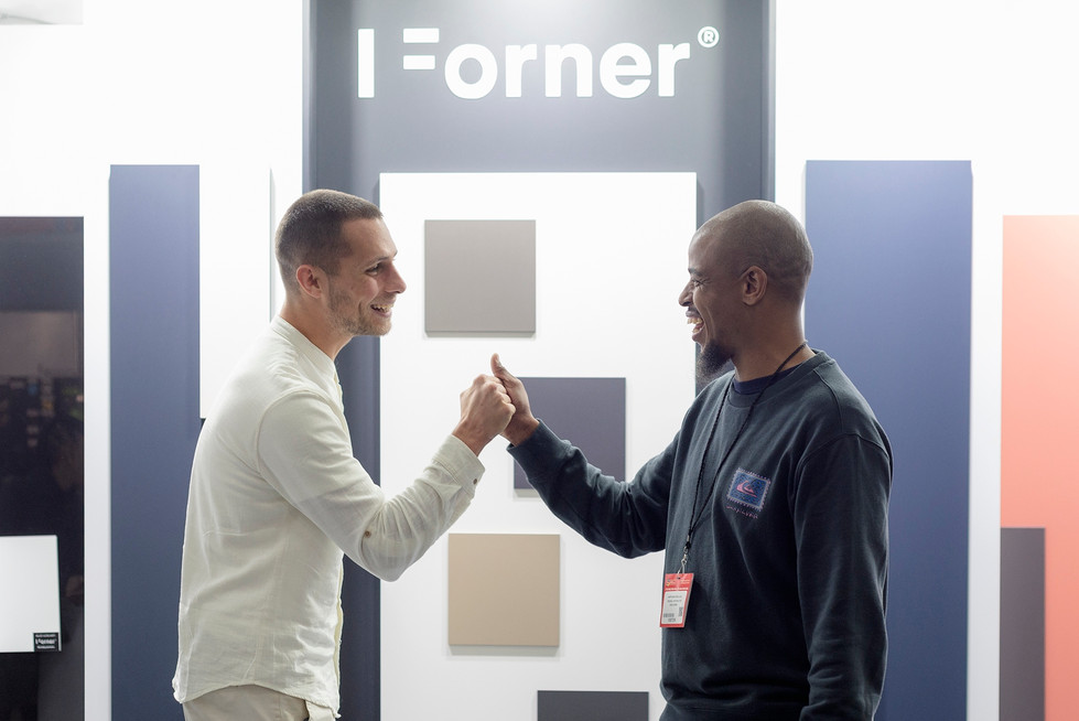 Twee mannen doen vuistbump bij I=Forner® stand met kleurstalen.