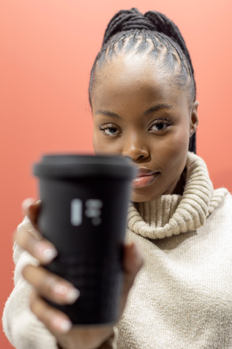 Jonge vrouw in crème trui toont zwarte beker, kijkt direct aan.