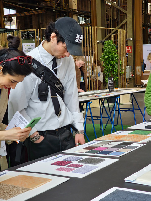 Twee mensen bekijken geïnteresseerd diverse materialenstalen op een beursstand.