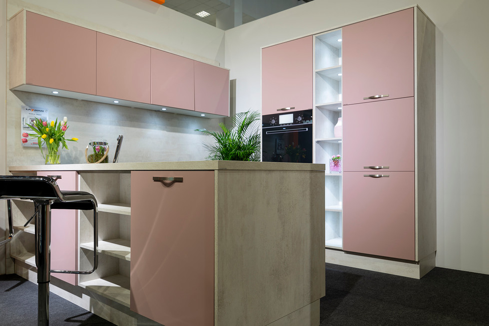 Roze moderne keuken met eiland, ingebouwde oven en groene plant.