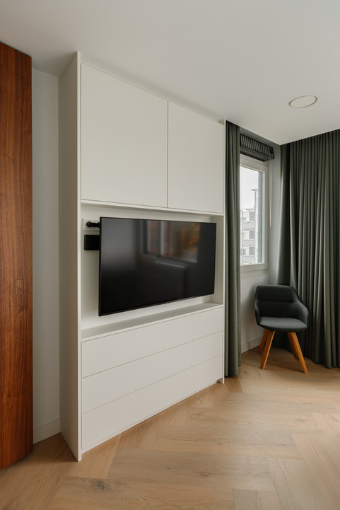 Witte ingebouwde kast met televisie, ladeblok en moderne stoel in kamer.
