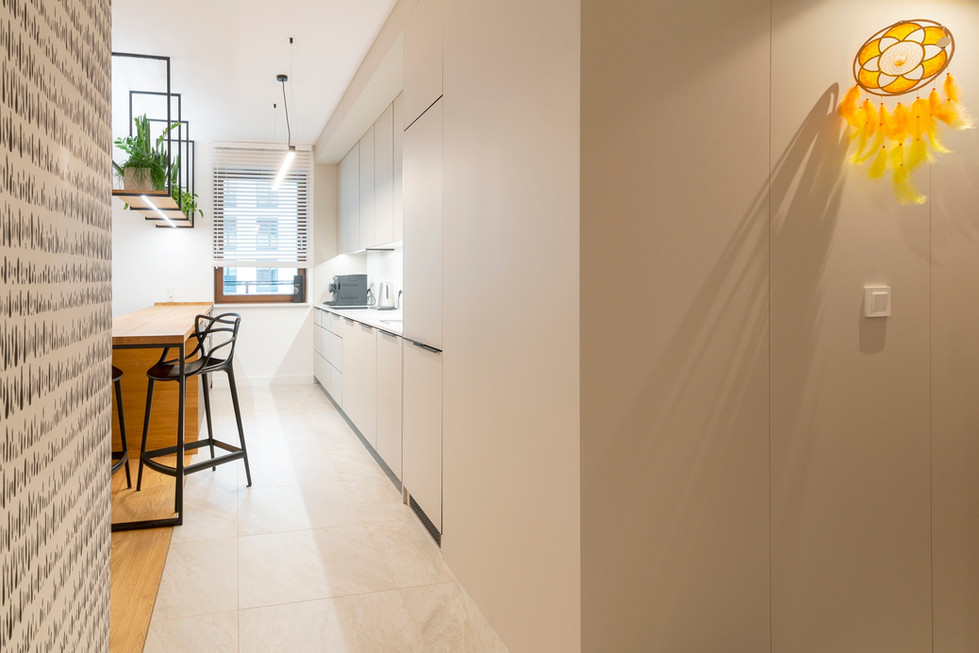 Lange, moderne keuken met lichte kasten, houten aanrecht en barstoel.