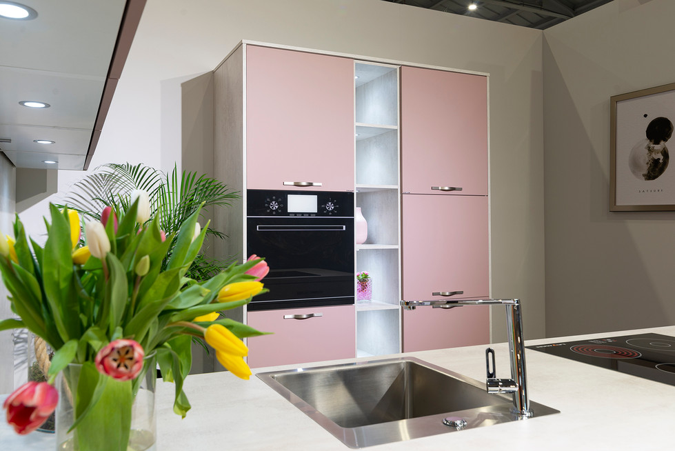 Moderne keuken met roze kasten, zwarte oven, gootsteen en tulpen.