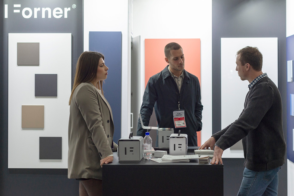 Drie mensen bespreken producten op beursstand met 'er' logo en witte kubussen.
