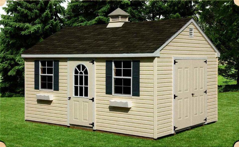 Beige storage shed with dark shingle roof, two front windows with black shutters, small white flower boxes, an arched door window in the center, and a larger double door on the right side, surrounded by grass and trees.