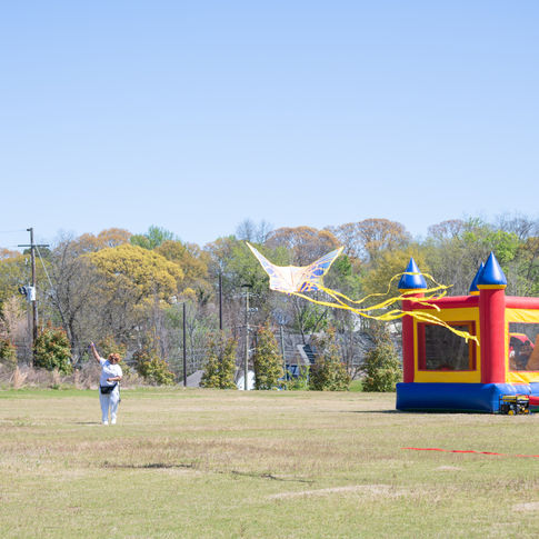 Two women work to get a kite in the air with a bounce house in the background