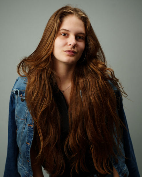 Allyn Raney poses confidently in a studio wearing a denim jacket and hoop earrings.