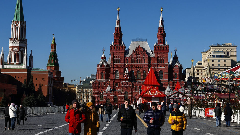 People walk in Red Square, Moscow, with the State Historical Museum in the background. Bright winter clothing and a clear blue sky.