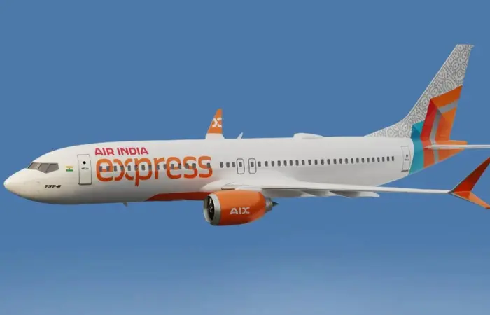White airplane with "Air India Express" in red and orange, flying against a blue sky. Tail features decorative patterns and orange accents.